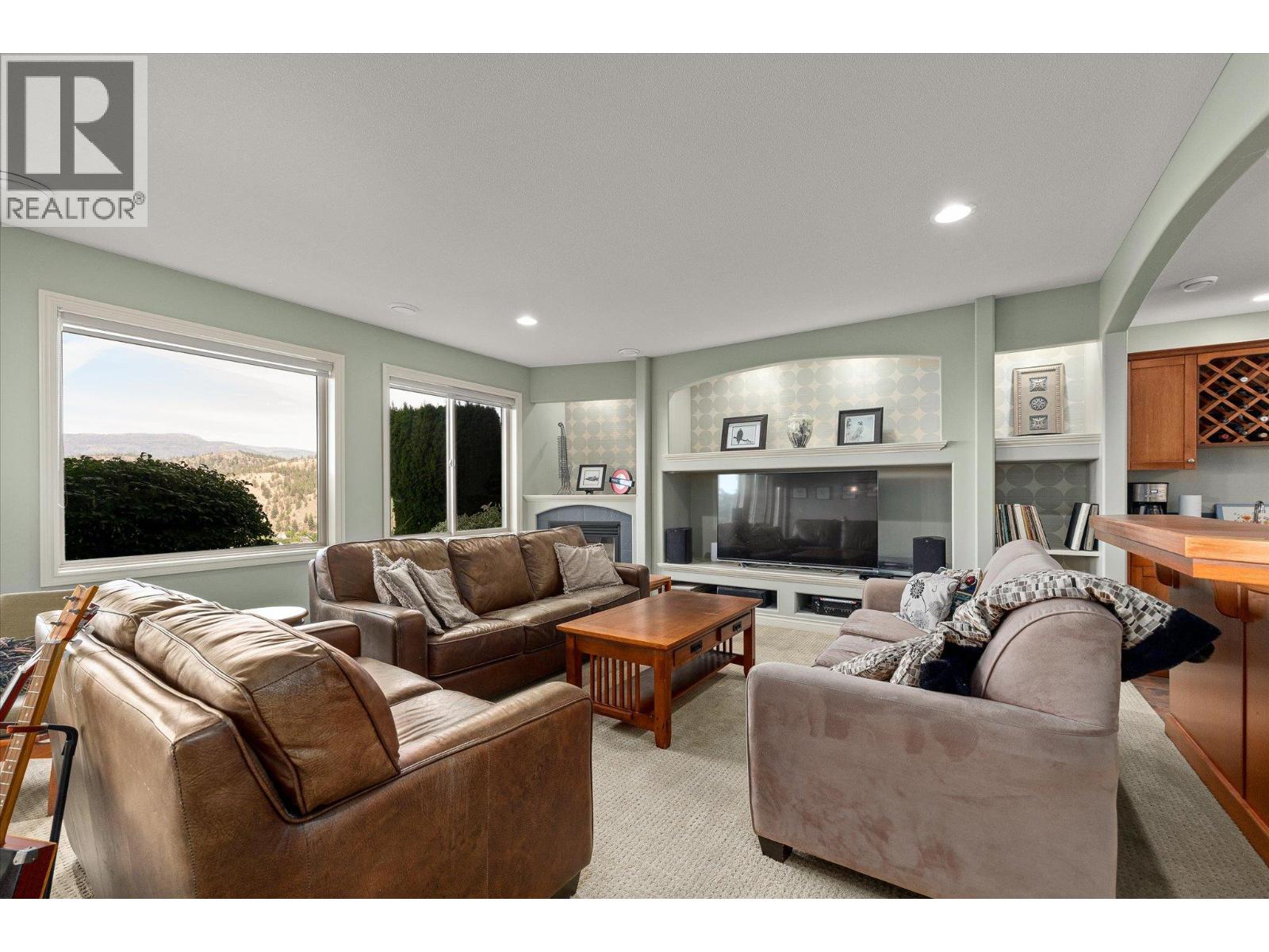 Furnished living room with leather sofas, built-in entertainment center, and windows overlooking a wooded hillside.
