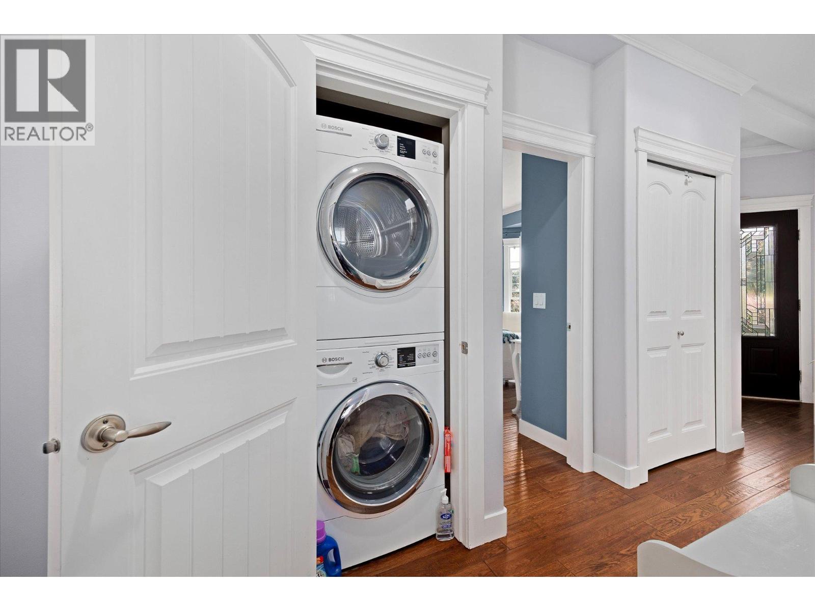 Laundry area with stacked Bosch washer and dryer in a white-trimmed closet beside a hardwood-floored hallway.