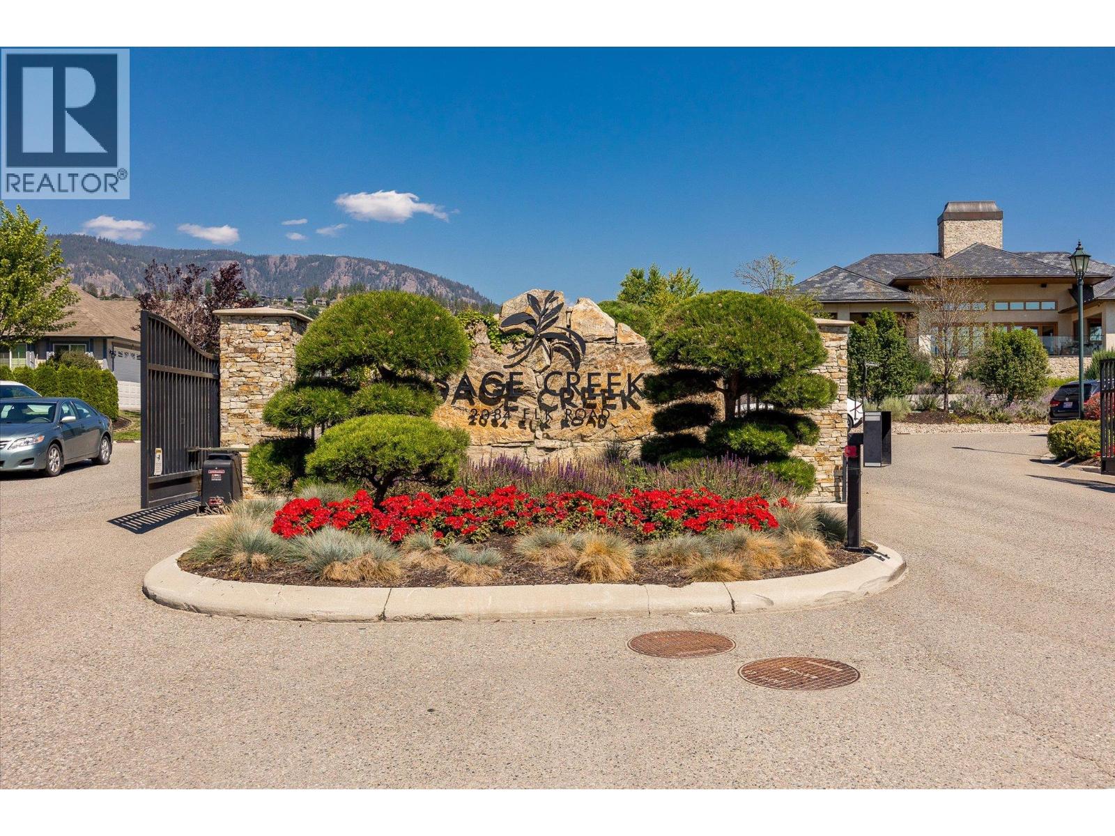 Sage Creek community entrance with a stone sign, landscaped flower beds, and homes beyond the gate.