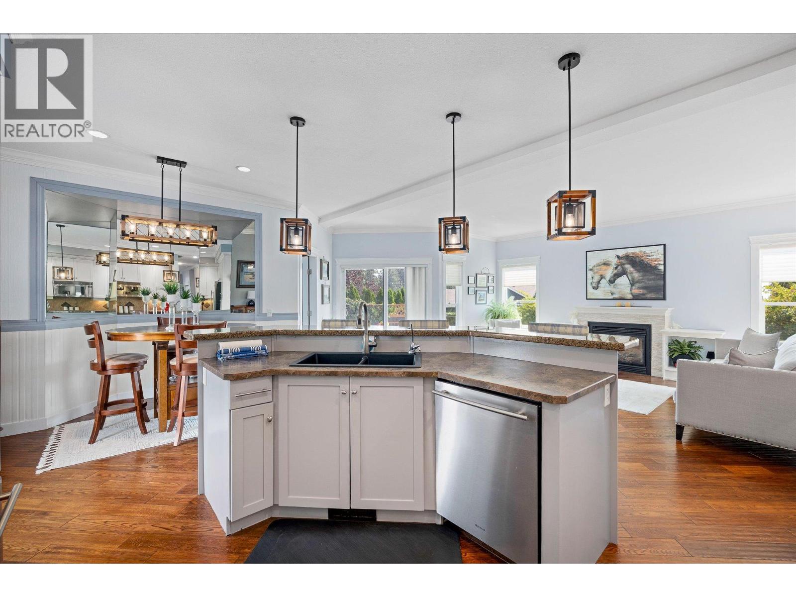 Open-plan kitchen with a large island, stone counters, pendant lights, and a view of the living room.