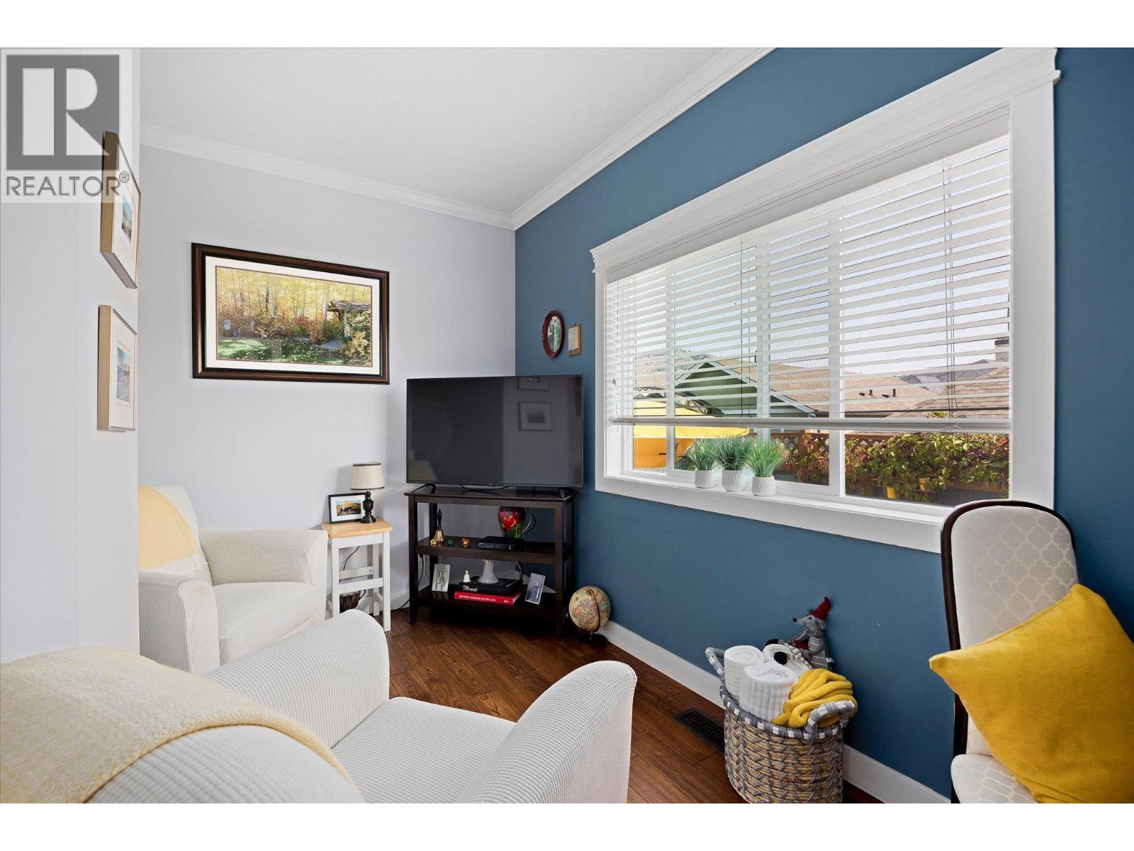 Living room with blue accent wall, white seating, television, and large window with blinds.