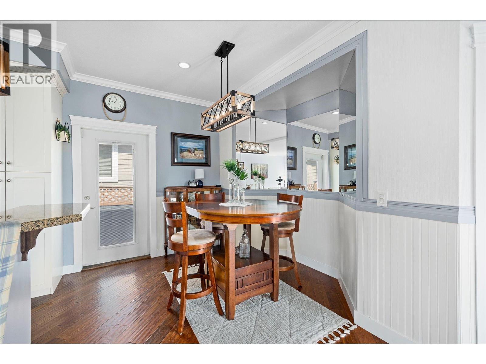 Dining area with a round wooden table, geometric pendant light, and large wall mirror.