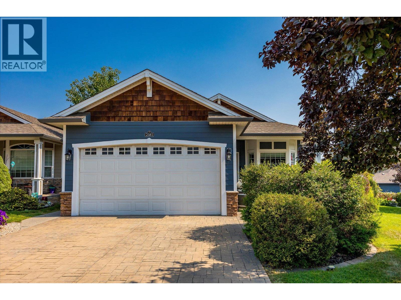 Home exterior with blue siding, a white double garage door, and a wide paved driveway.