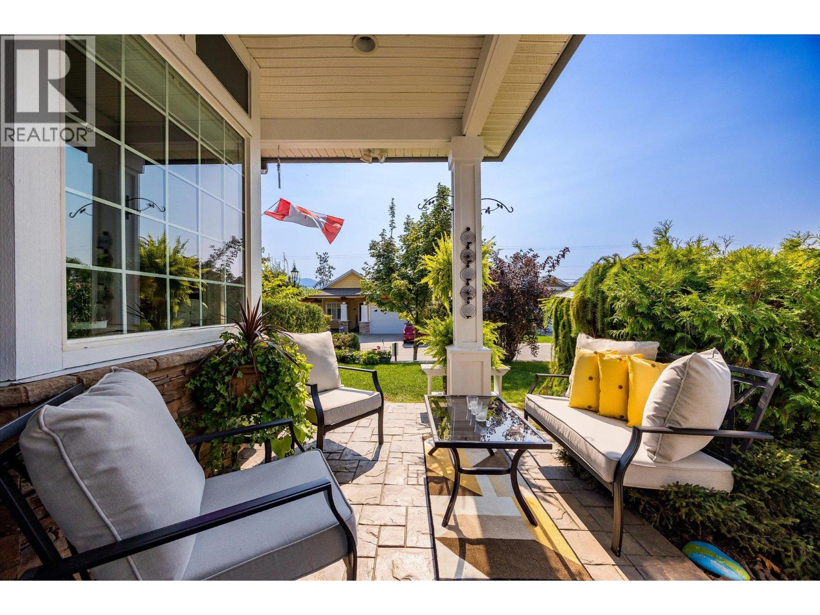 Covered patio with cushioned seating, stone pavers, and leafy garden views.
