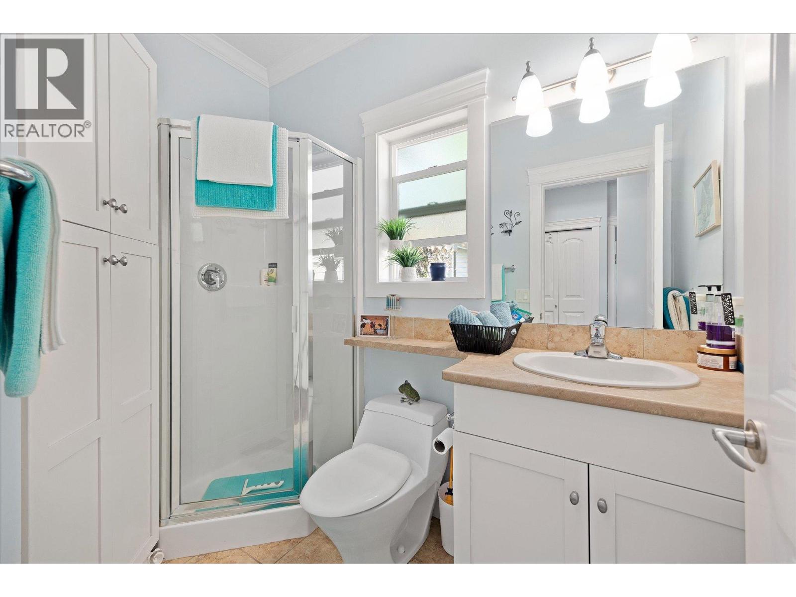 Bathroom with a glass shower, white cabinetry, tan vanity countertop, and turquoise towels.
