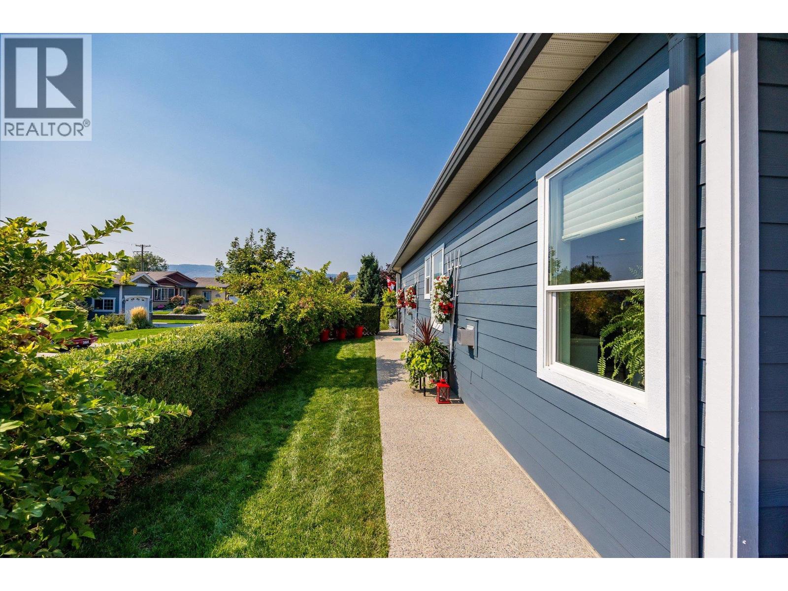 Blue home’s side yard with a concrete walkway, trimmed lawn, hedges, and flower planters.