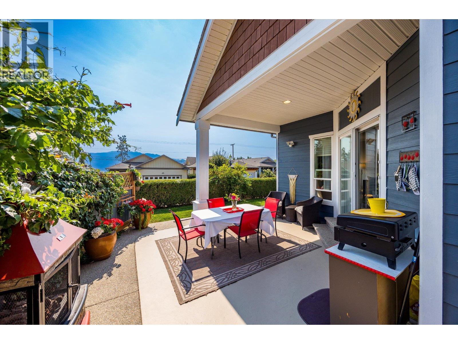 Covered patio with red dining chairs, an outdoor grill, flower planters, and distant mountain views.