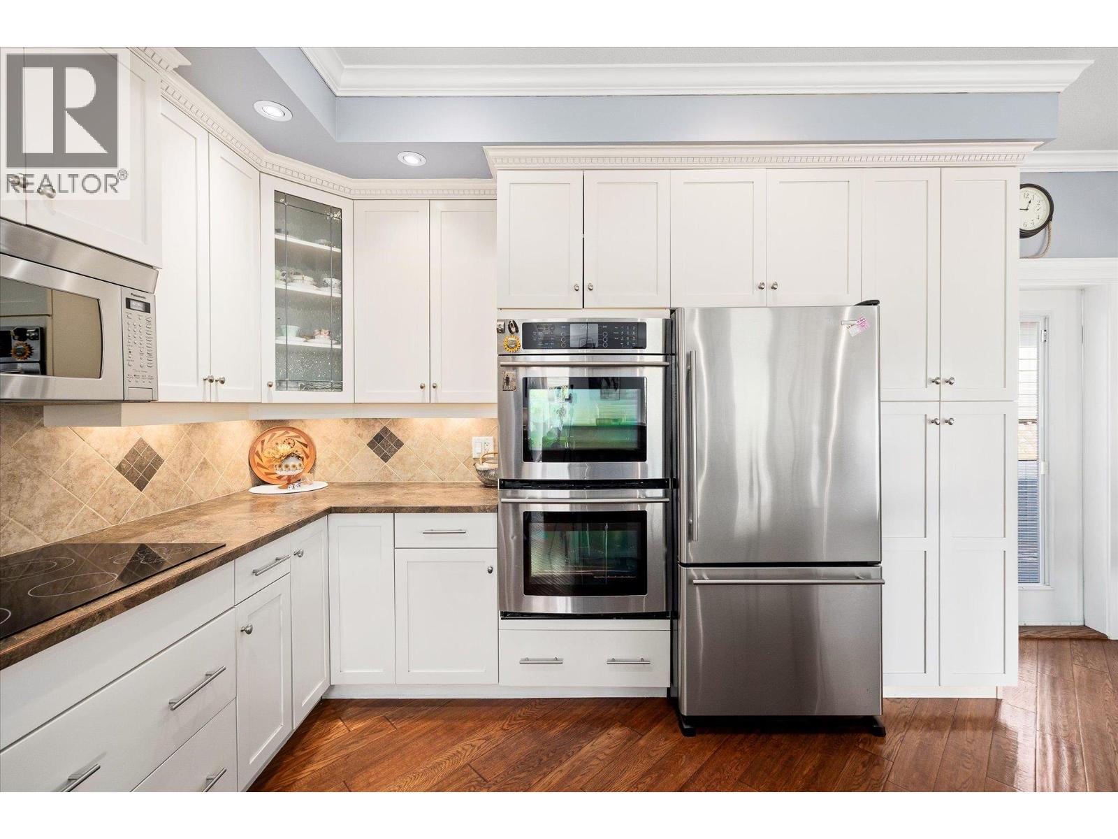 Bright kitchen with white cabinetry, stainless steel appliances, tile backsplash, and hardwood flooring.