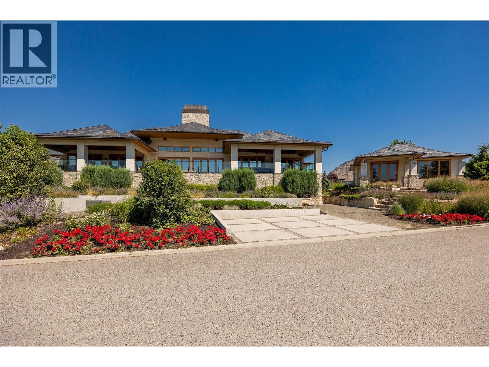 Large stone-accented home with covered patios, a paved driveway, and colorful landscaped flower beds.