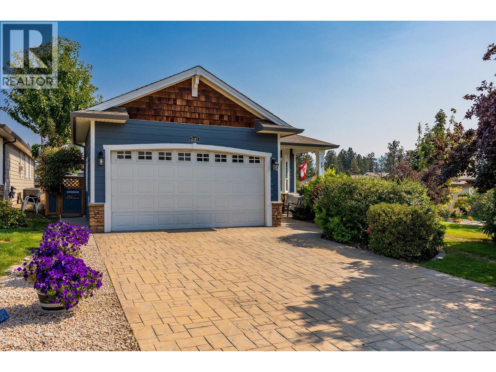 Blue home with a double garage, broad paved driveway, and landscaped flower beds.