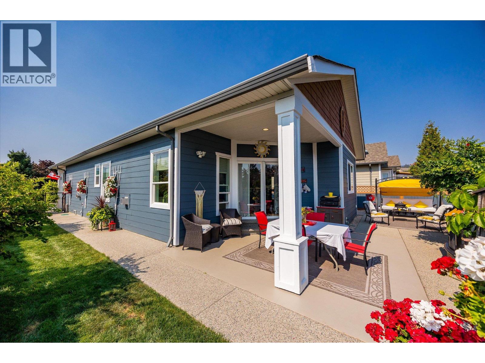 Blue single-story home with a covered patio, outdoor dining set, and yellow-canopied lounge.