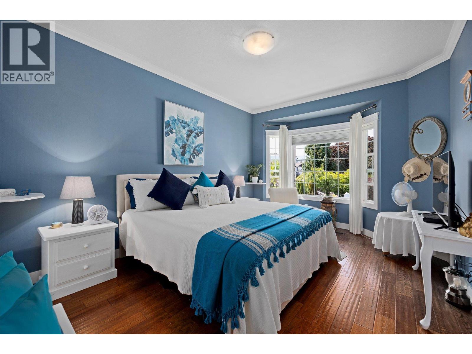 Bedroom with blue walls, a white bed, turquoise throw, and large window overlooking greenery.