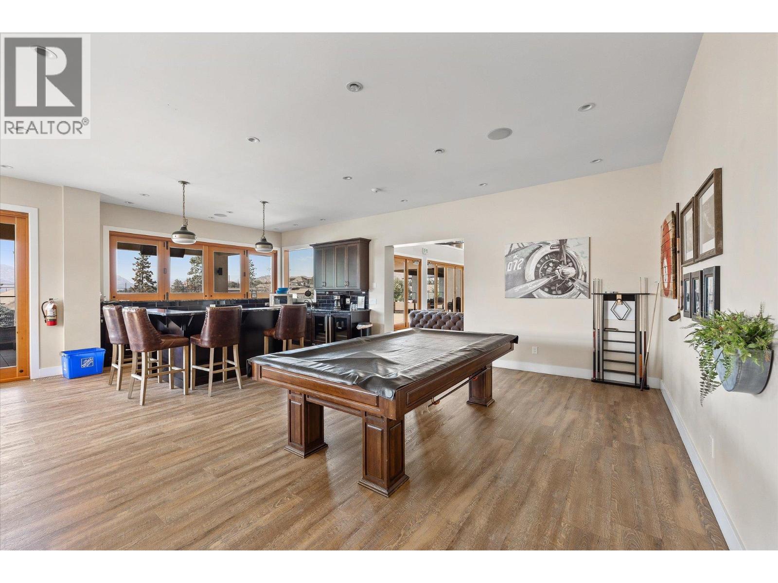 Recreation room with a large pool table, bar seating, dark cabinetry, and wood-framed windows.
