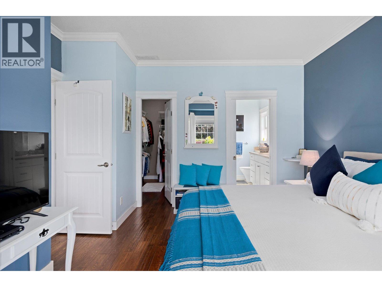 Bedroom with a white bed and turquoise bedding, pale blue walls, and open closet and bathroom doors.