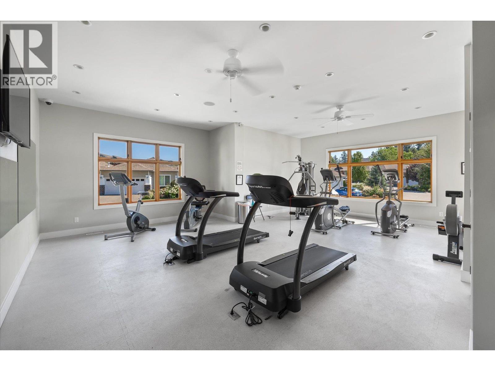 Fitness room with treadmills and cardio equipment beside large windows.