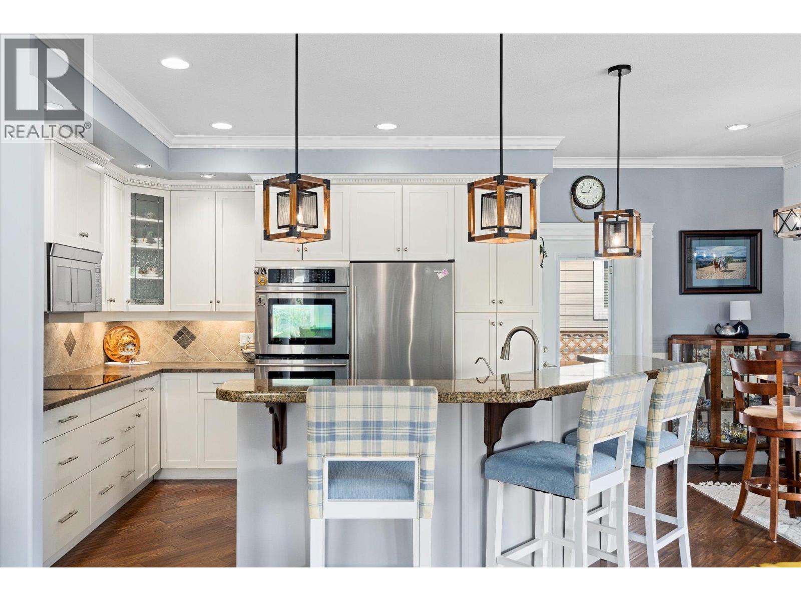 Kitchen with white cabinets, stainless steel appliances, and a granite island with bar seating.