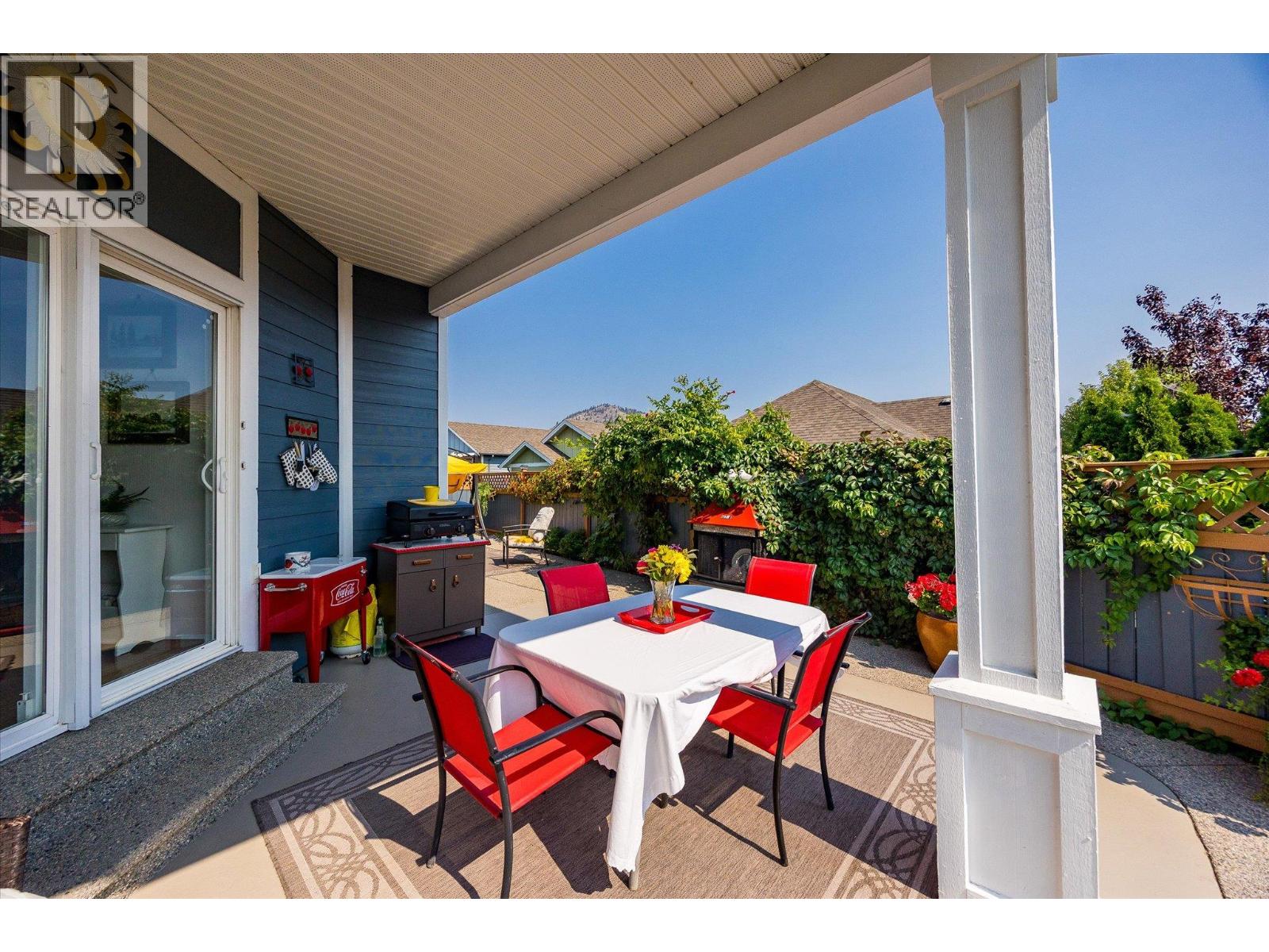 Covered patio with red dining chairs, a barbecue, and a leafy privacy hedge.