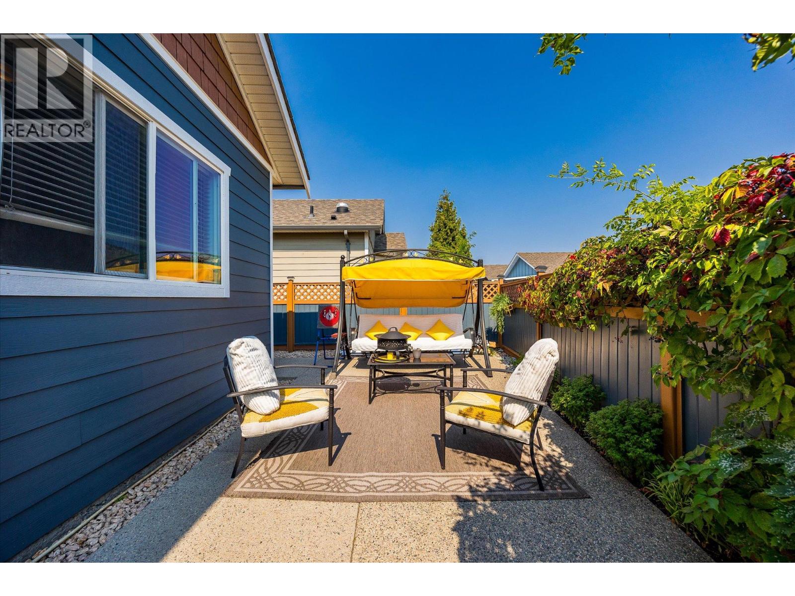 Backyard patio with cushioned chairs, a yellow-canopy swing, and leafy vines along the fence.