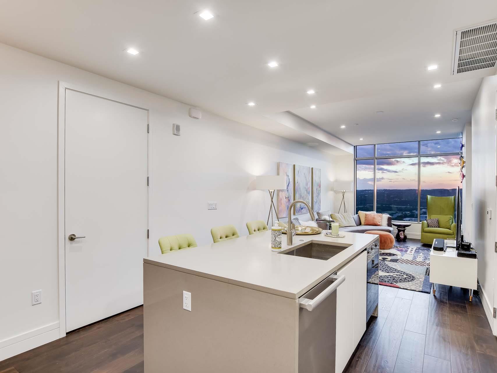 Open-plan condo kitchen and living room with a large island and city views at dusk.