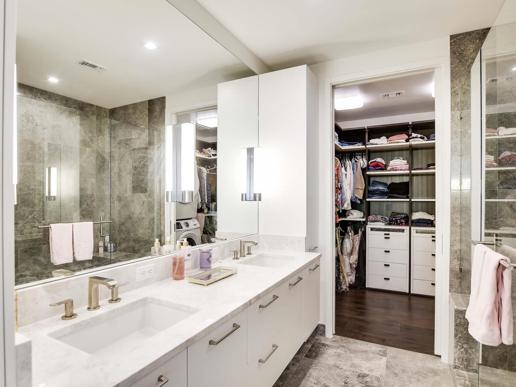 Modern bathroom with a white double vanity and gray stone tile beside an open walk-in closet.