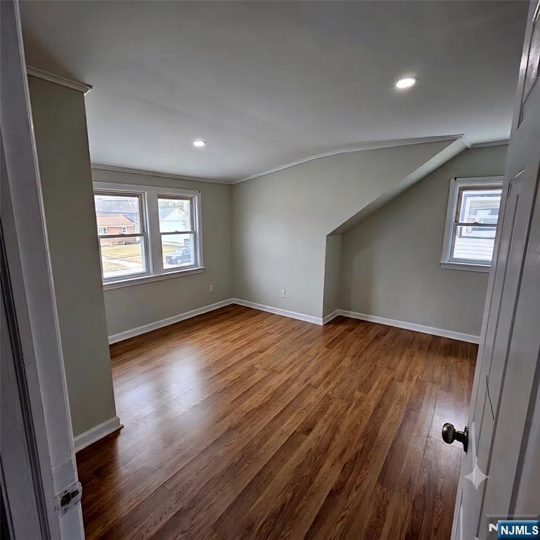 Empty room with hardwood floors, three windows, and a sloped ceiling nook.