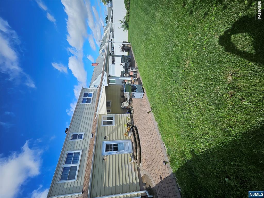 Two-story house with a covered, furnished patio and brick paving beside a broad green lawn.