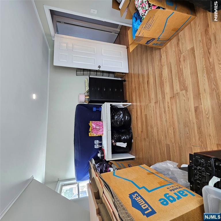 Cluttered room with wood-look flooring, moving boxes, a dresser, and covered furniture.