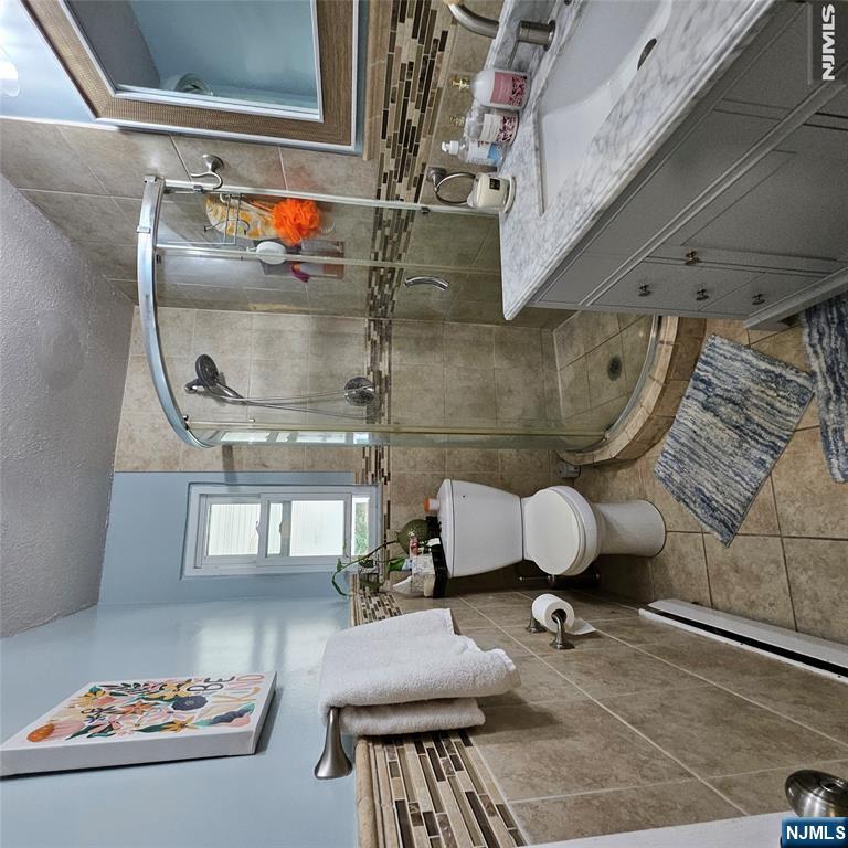 Bathroom with a curved glass shower, beige tile, and a gray vanity with a marble-look countertop.