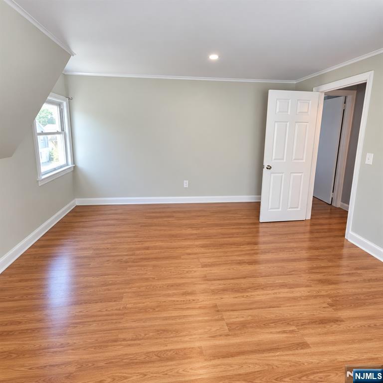 Empty room with warm-toned wood flooring, light gray walls, and an open door.