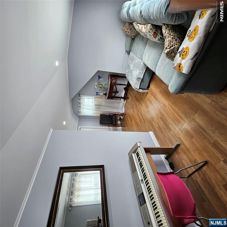 Living room with a gray sectional, digital piano, pink chair, and warm wood flooring.