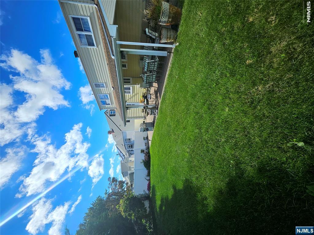 Backyard lawn and covered patio with outdoor dining furniture beside a two-story house.
