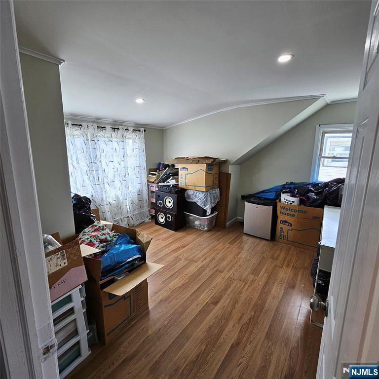 Upper-level room with a sloped ceiling, wood-look flooring, and boxes stored around the edges.