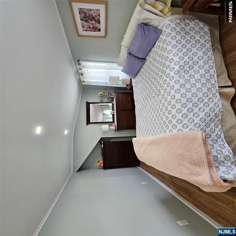 Bedroom with a patterned bedspread, lavender pillows, dark wood dressers, and hardwood floors.