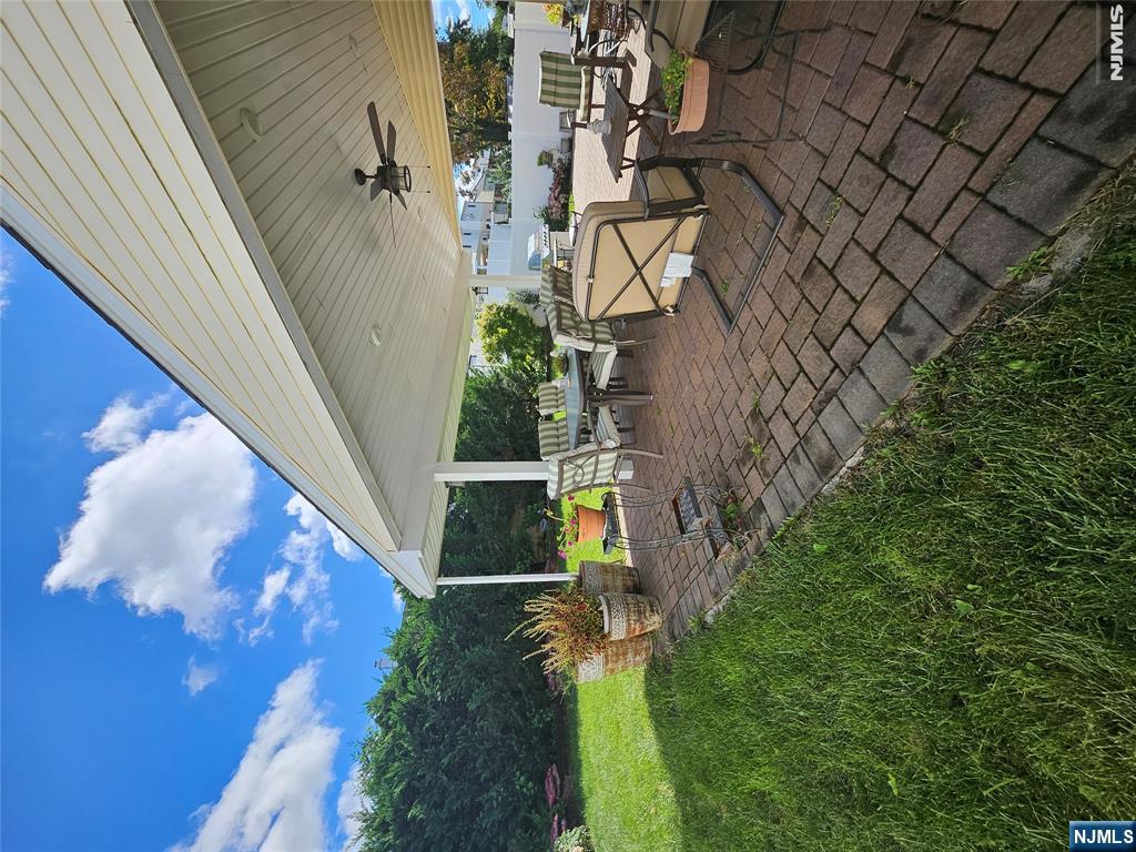 Covered brick patio with outdoor dining furniture and a ceiling fan beside a green lawn.