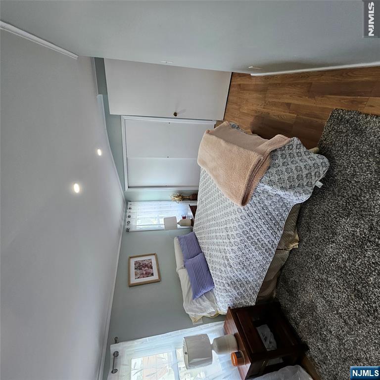 Furnished bedroom with purple pillows, patterned bedding, hardwood floors, and sliding closet doors.