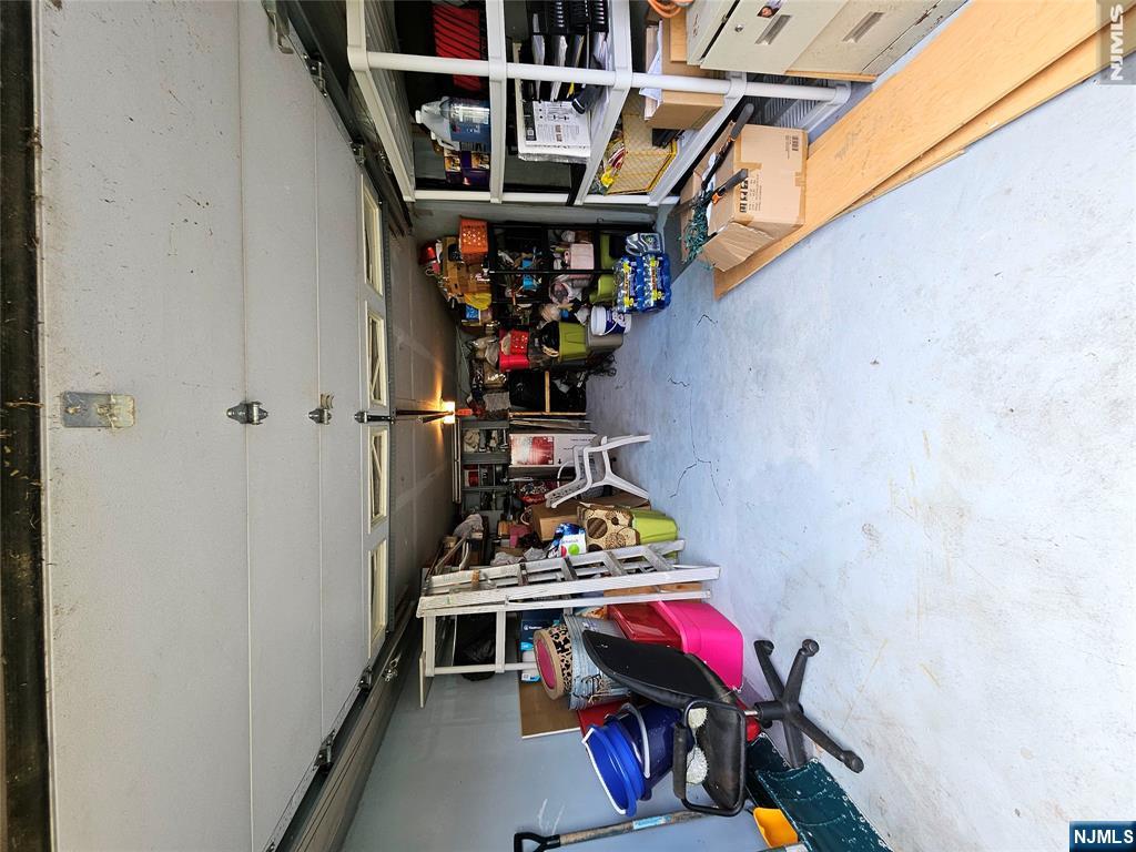 Garage with an open overhead door, concrete floor, and storage shelves filled with household items.