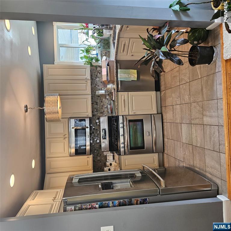 Kitchen with cream cabinets, stainless steel appliances, and a mosaic tile backsplash.