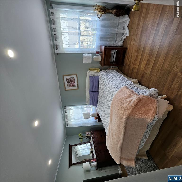 Furnished bedroom with a large bed, peach throw, dark wood dresser, and sheer-curtained windows.