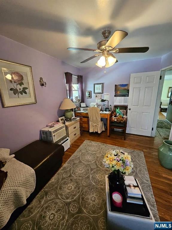 Furnished home office with lavender walls, a desk, ceiling fan, and patterned rug.