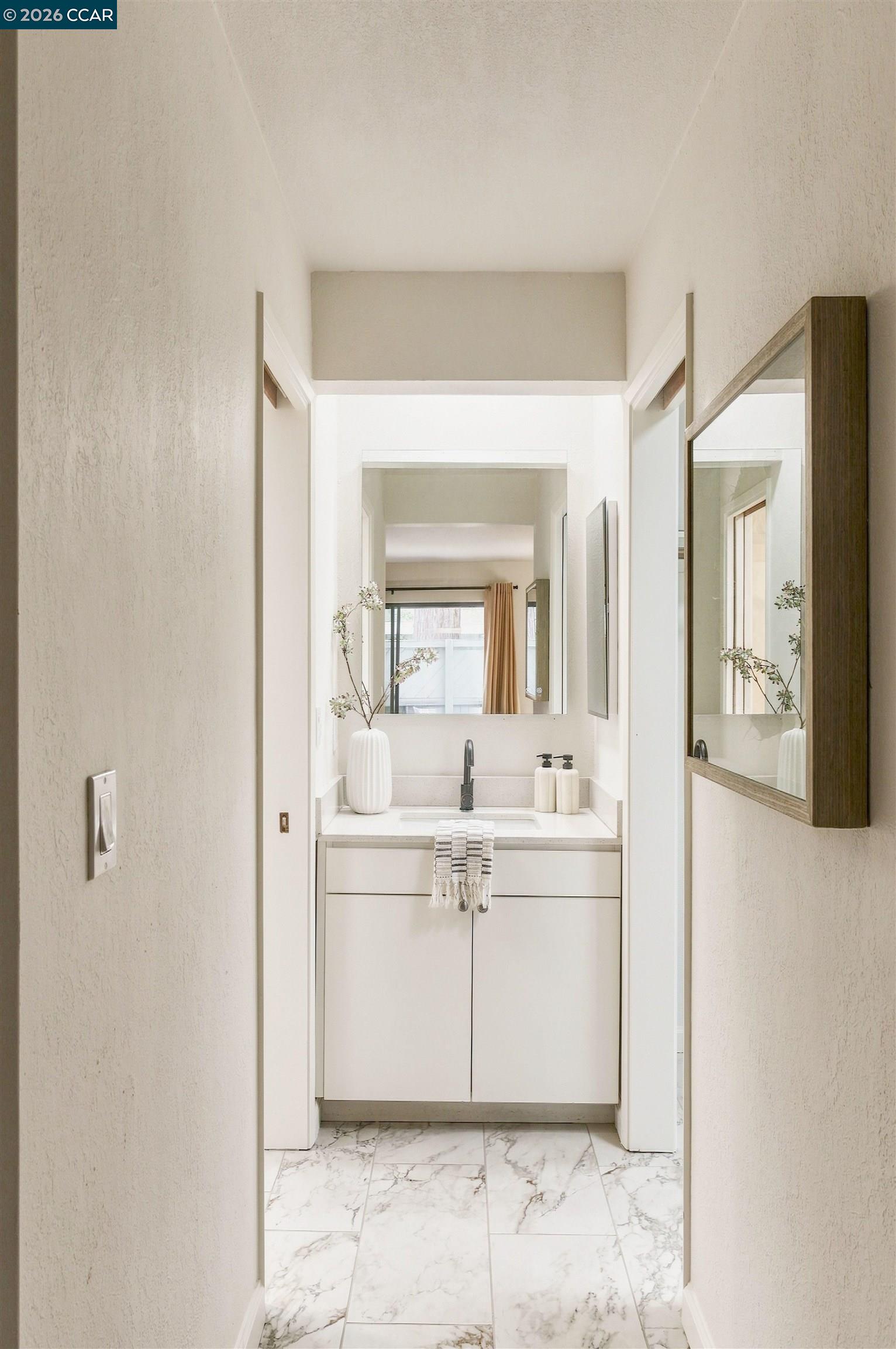 Bathroom vanity with a large mirror, white cabinetry, and marble-look floor tiles.