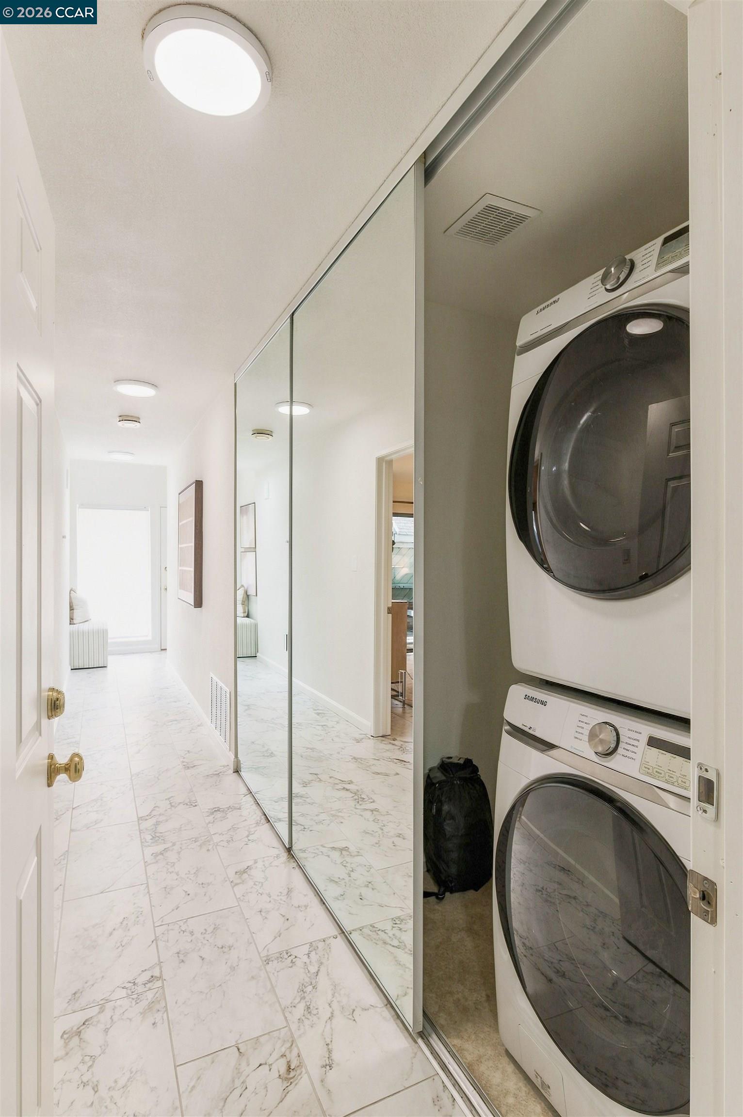 Hallway with marble-look tile and mirrored doors beside a closet with stacked washer and dryer.