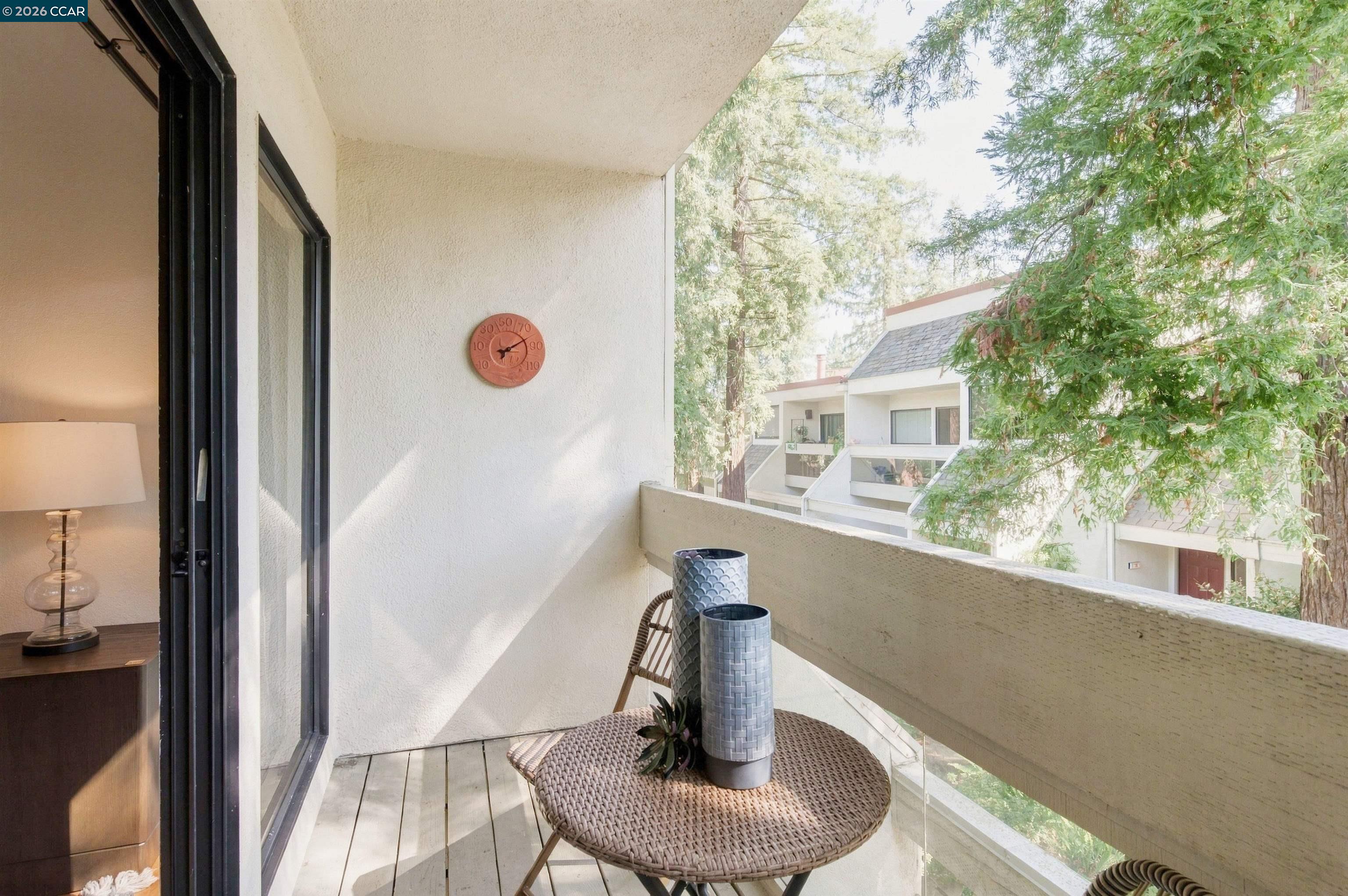 Furnished apartment balcony with a woven table and leafy views of neighboring condos.