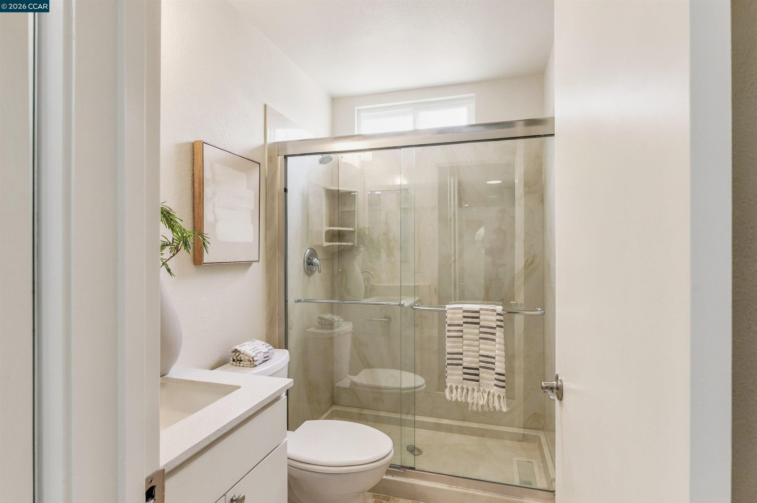 Bathroom with a glass-enclosed shower, built-in niche, white vanity, and folded towels.