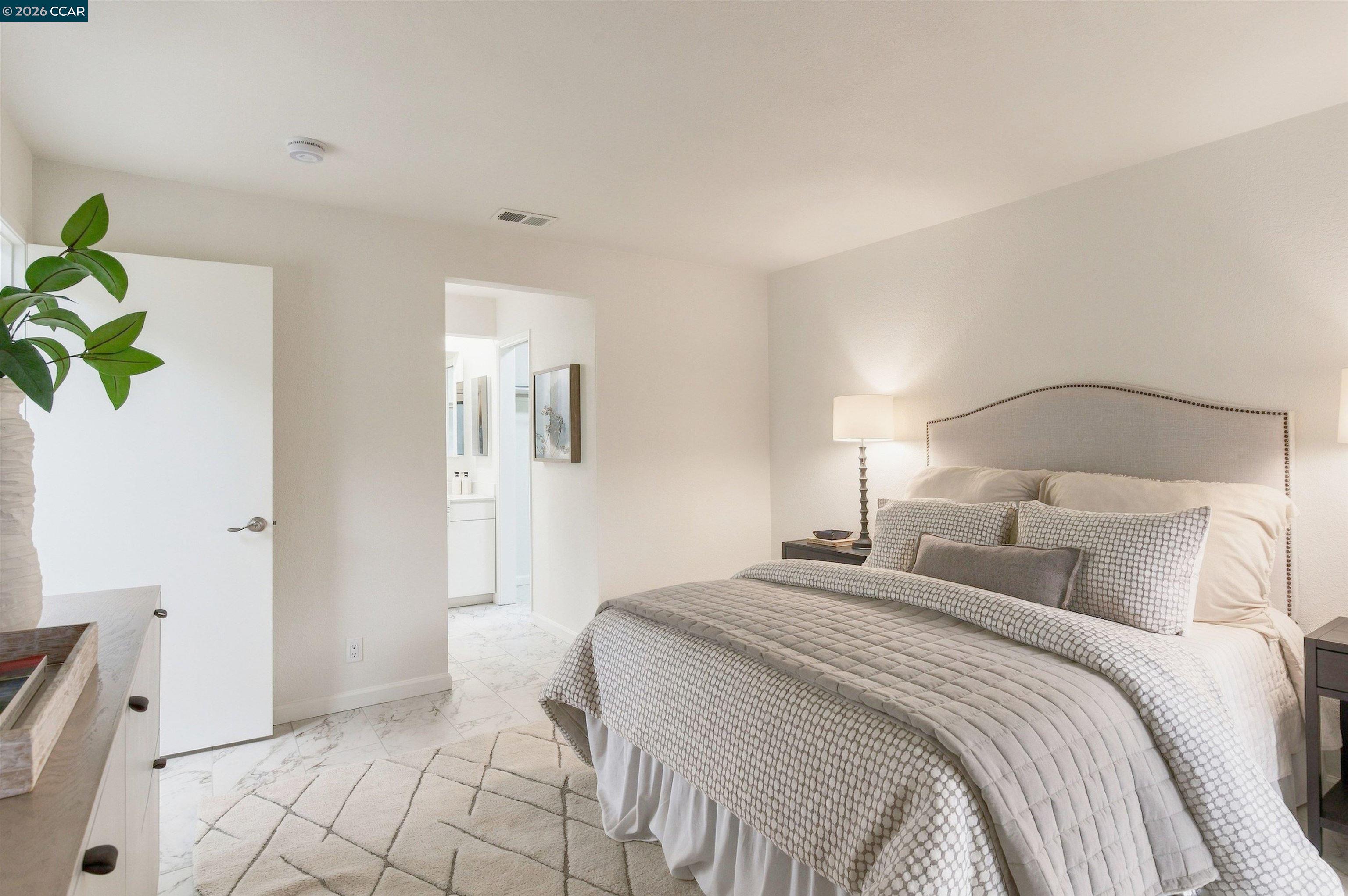 Furnished bedroom with a tall upholstered headboard and doorway to the bathroom.