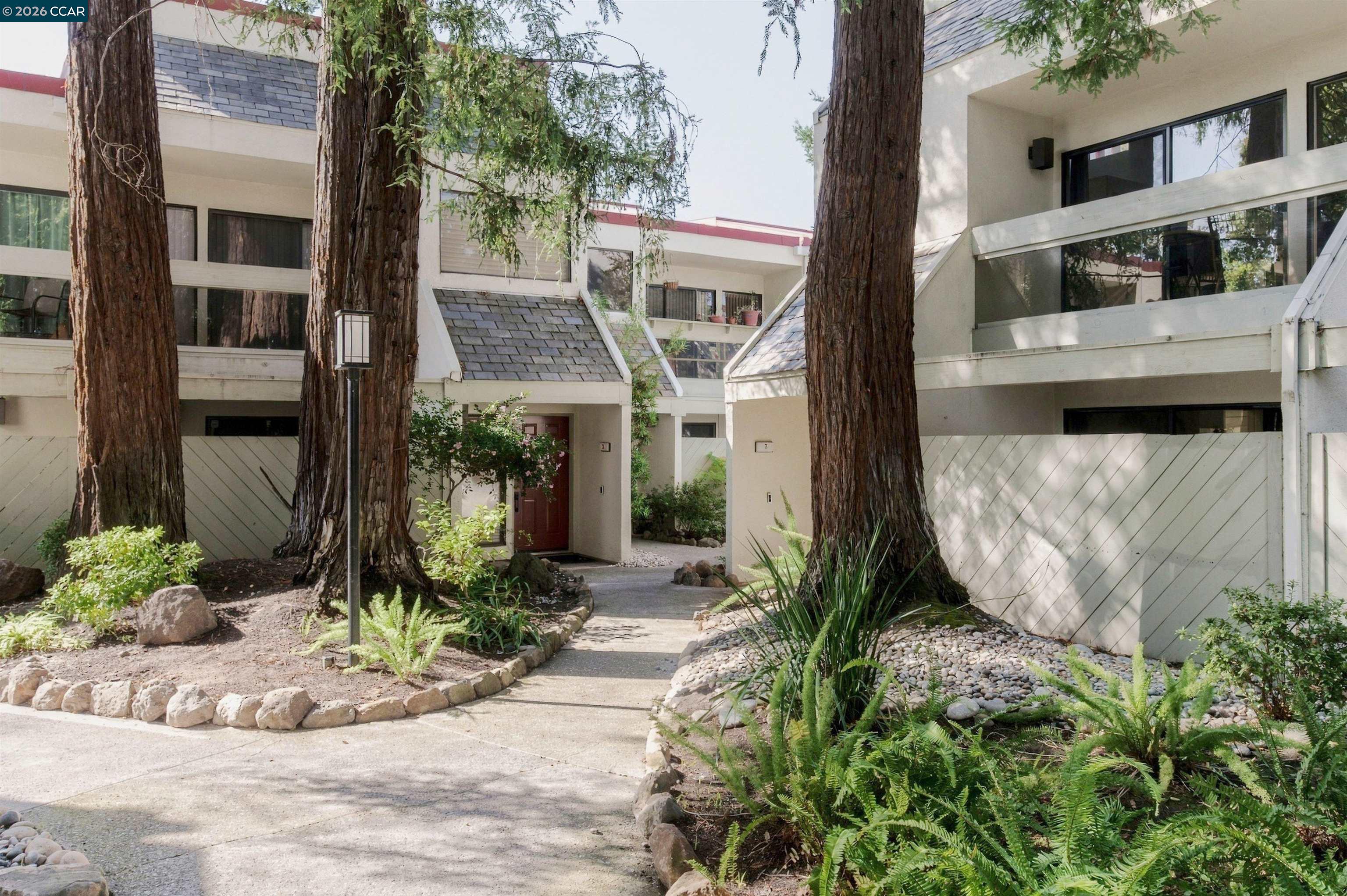 Condominium entrance with a red door, landscaped path, and mature trees.
