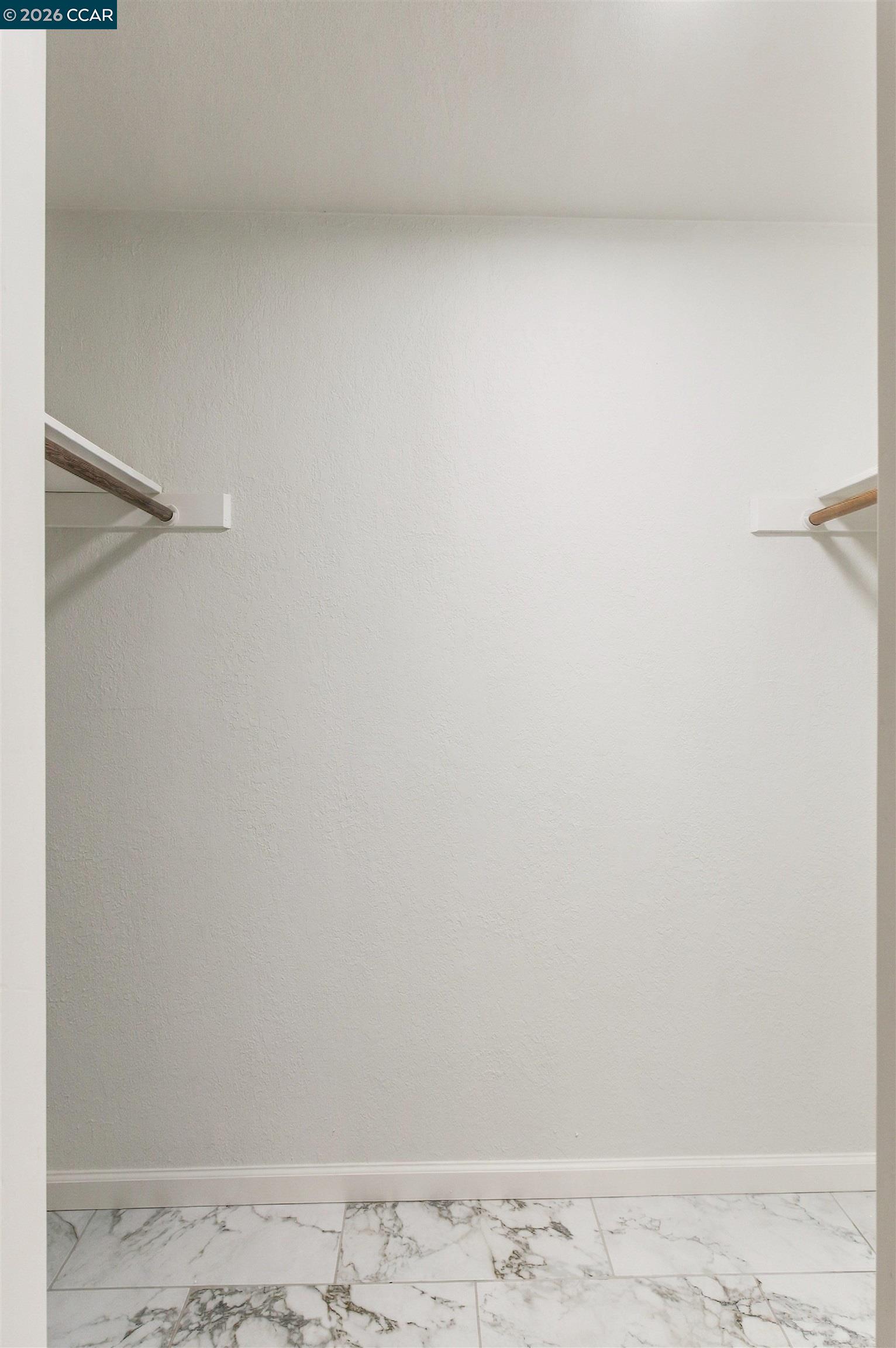 Empty walk-in closet with wooden hanging rods and marble-look tile flooring.