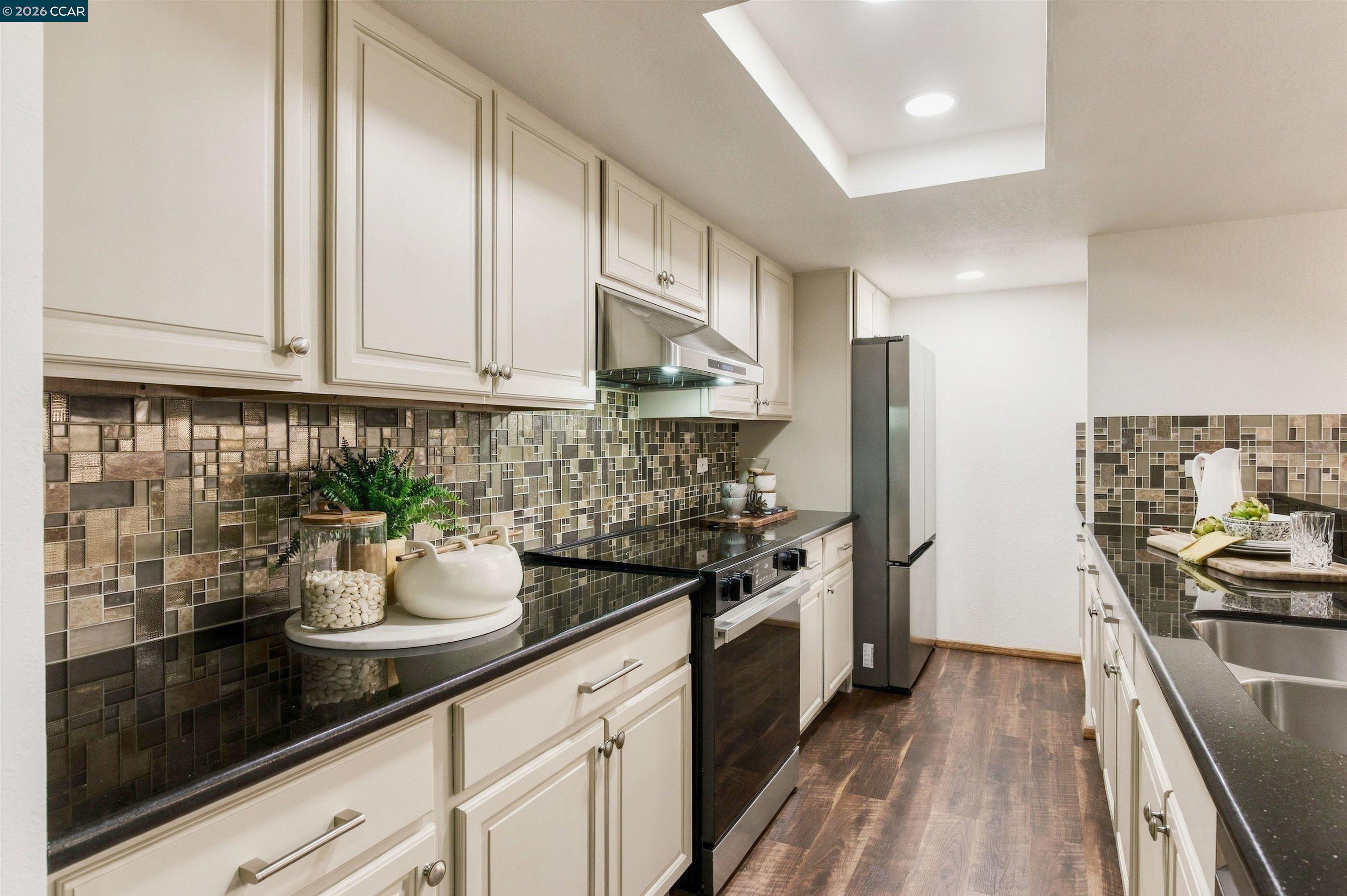Kitchen with cream cabinetry, mosaic tile backsplash, dark counters, and stainless steel appliances.