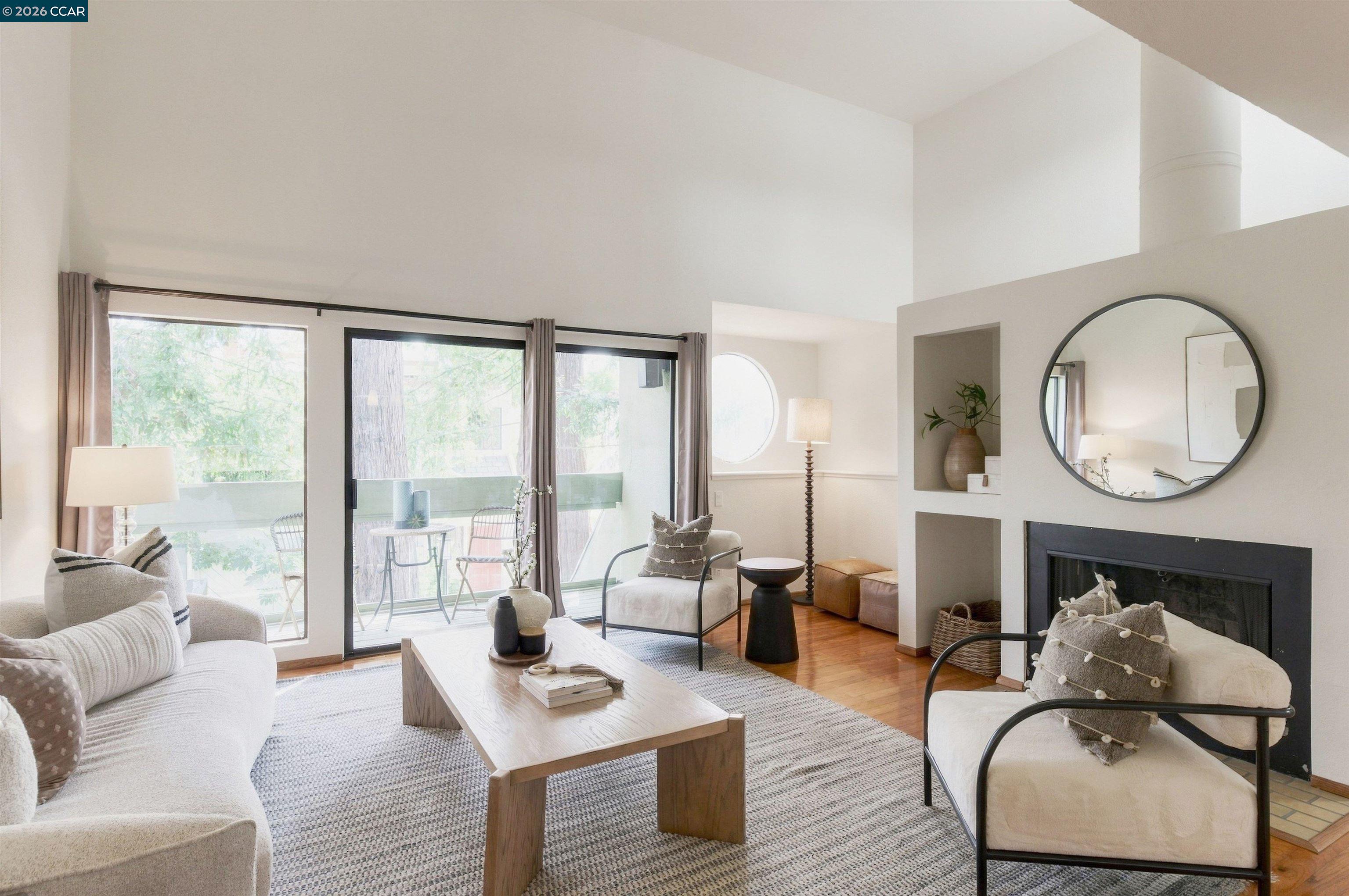 Bright living room with a high ceiling, fireplace, round mirror, and sliding doors to a balcony.