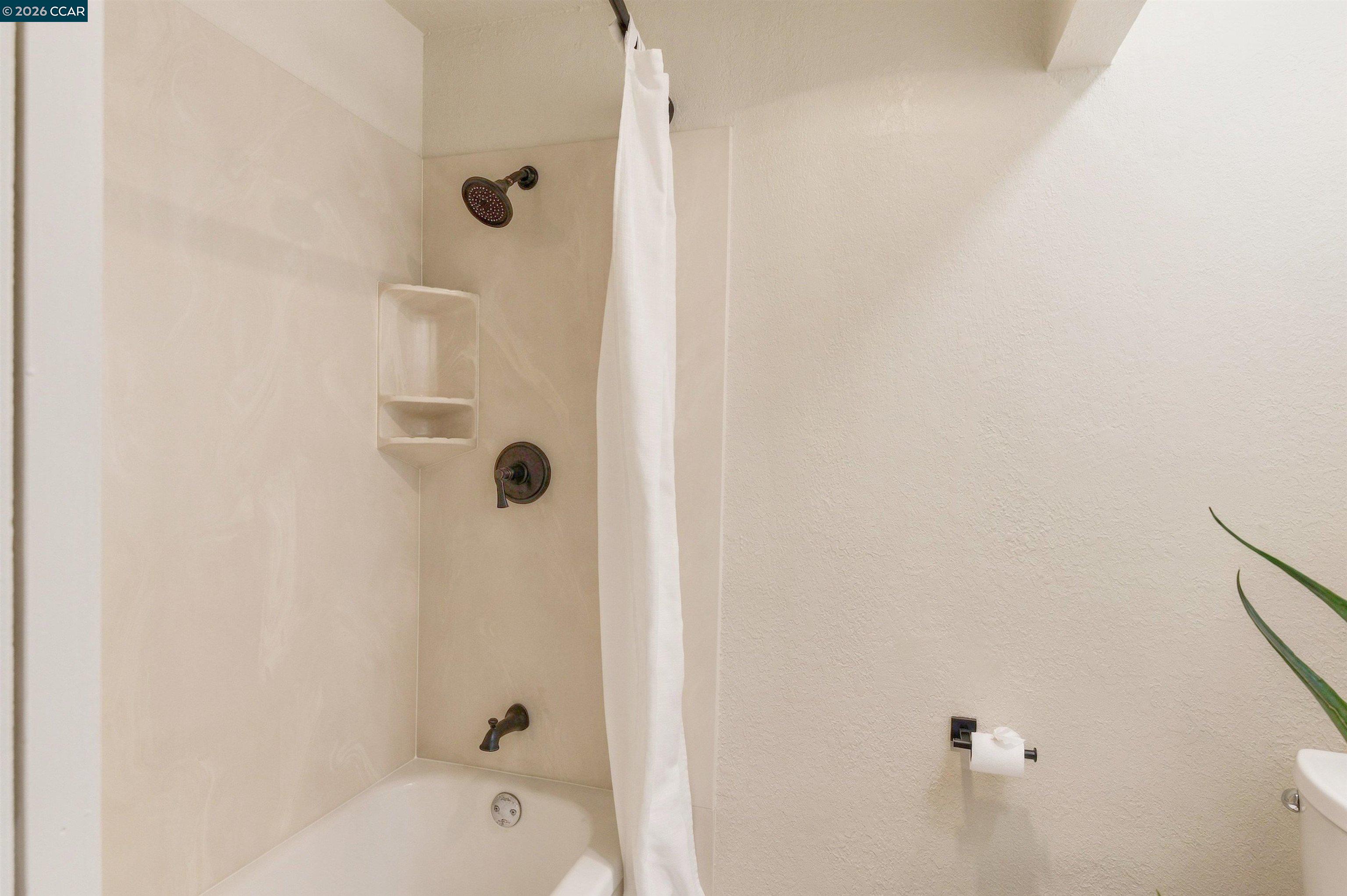 Bathroom with a bathtub, white shower curtain, built-in shower niche, and dark bronze fixtures.
