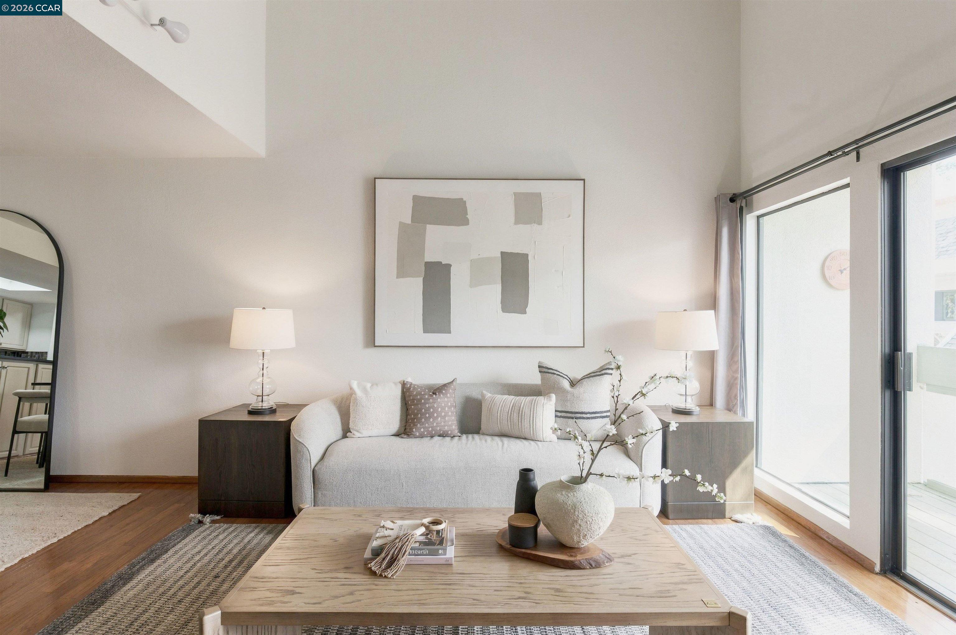 Staged living room with a light sofa, abstract artwork, wood coffee table, and sliding glass doors.